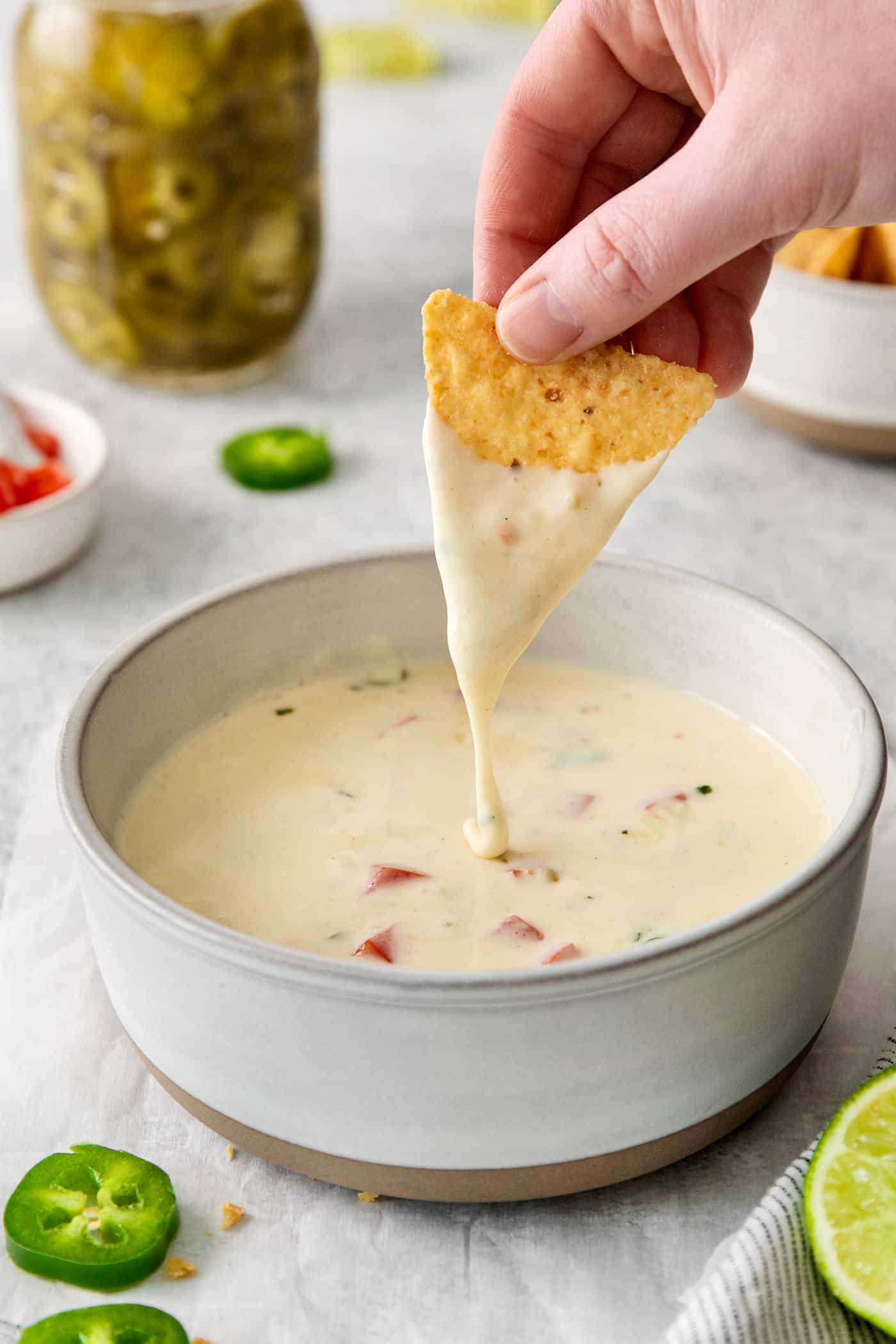 Smooth and creamy with just the right amount of heat, this Homemade Queso Blanco is made with just 5 ingredients! Quick & easy! A hand dipping a tortilla into queso blanco
