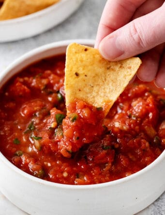 A hand dipping a chip into salsa