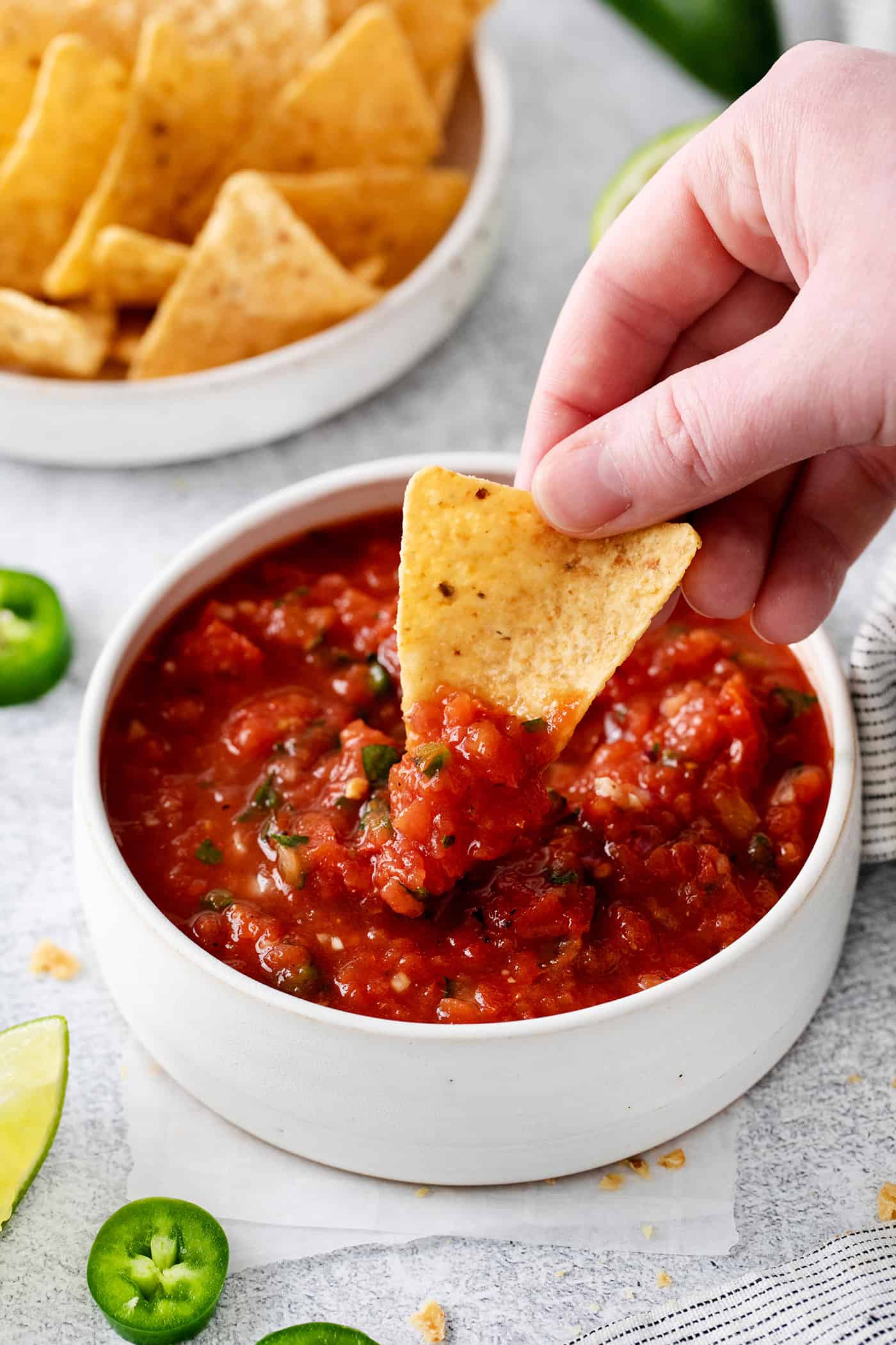 This Restaurant Style Salsa is a mild and easy salsa recipe made with fire-roasted tomatoes, jalapenos, cilantro, and Iime. A hand dipping a chip into restaurant style salsa