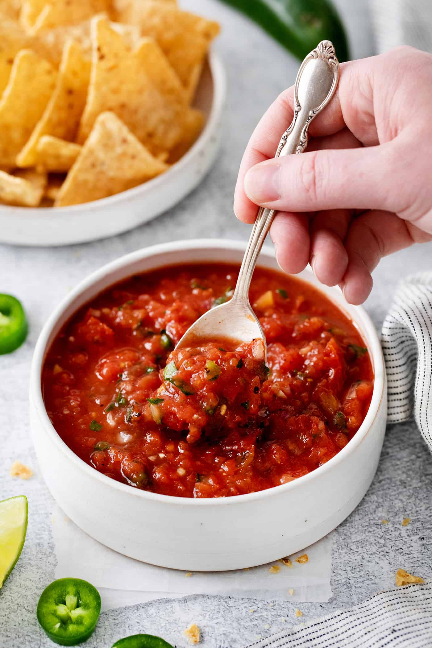 This Restaurant Style Salsa is a mild and easy salsa recipe made with fire-roasted tomatoes, jalapenos, cilantro, and Iime. A hand holding a spoon in a bowl of restaurant style salsa