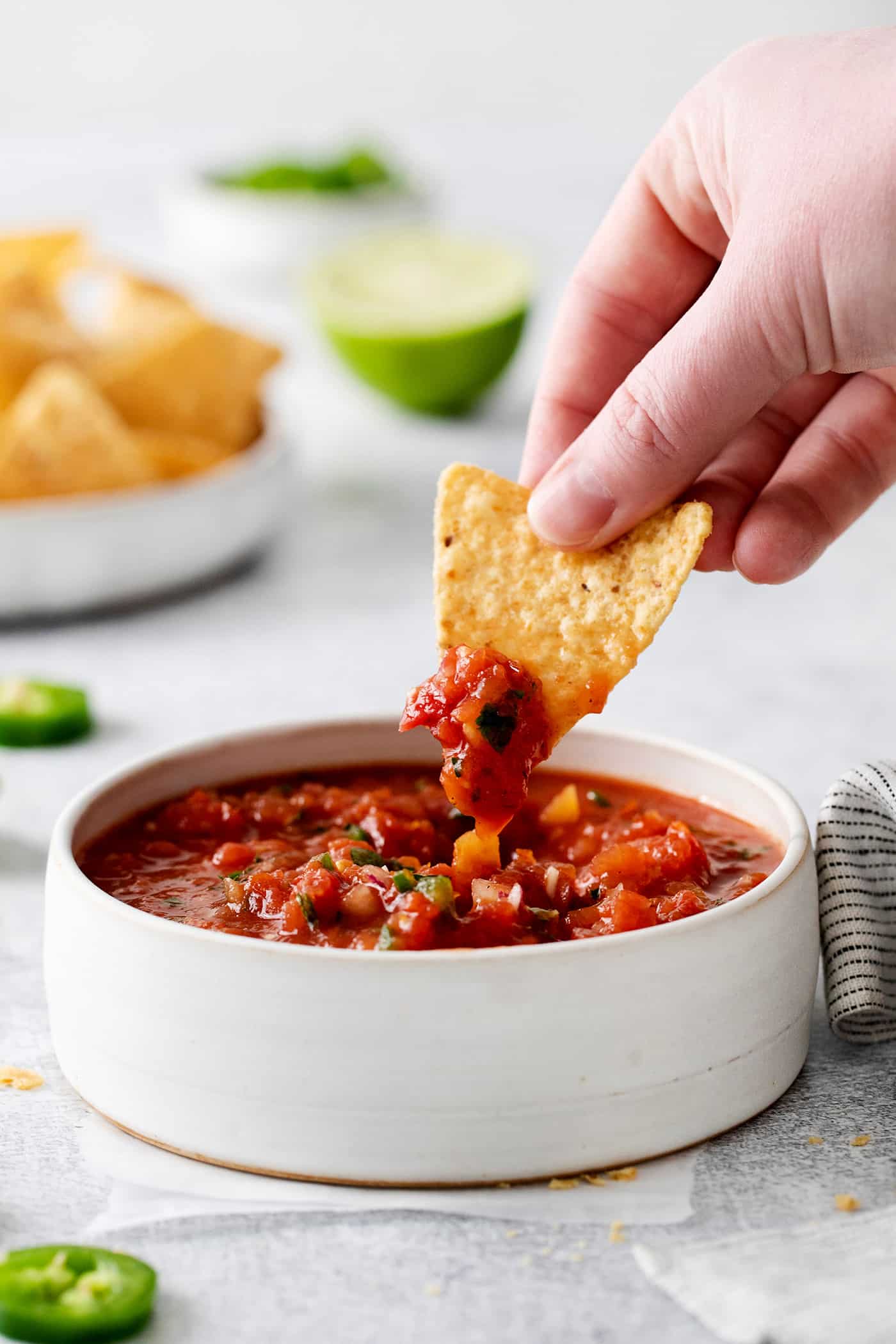 This Restaurant Style Salsa is a mild and easy salsa recipe made with fire-roasted tomatoes, jalapenos, cilantro, and Iime. A hand holding a chip dipped in salsa