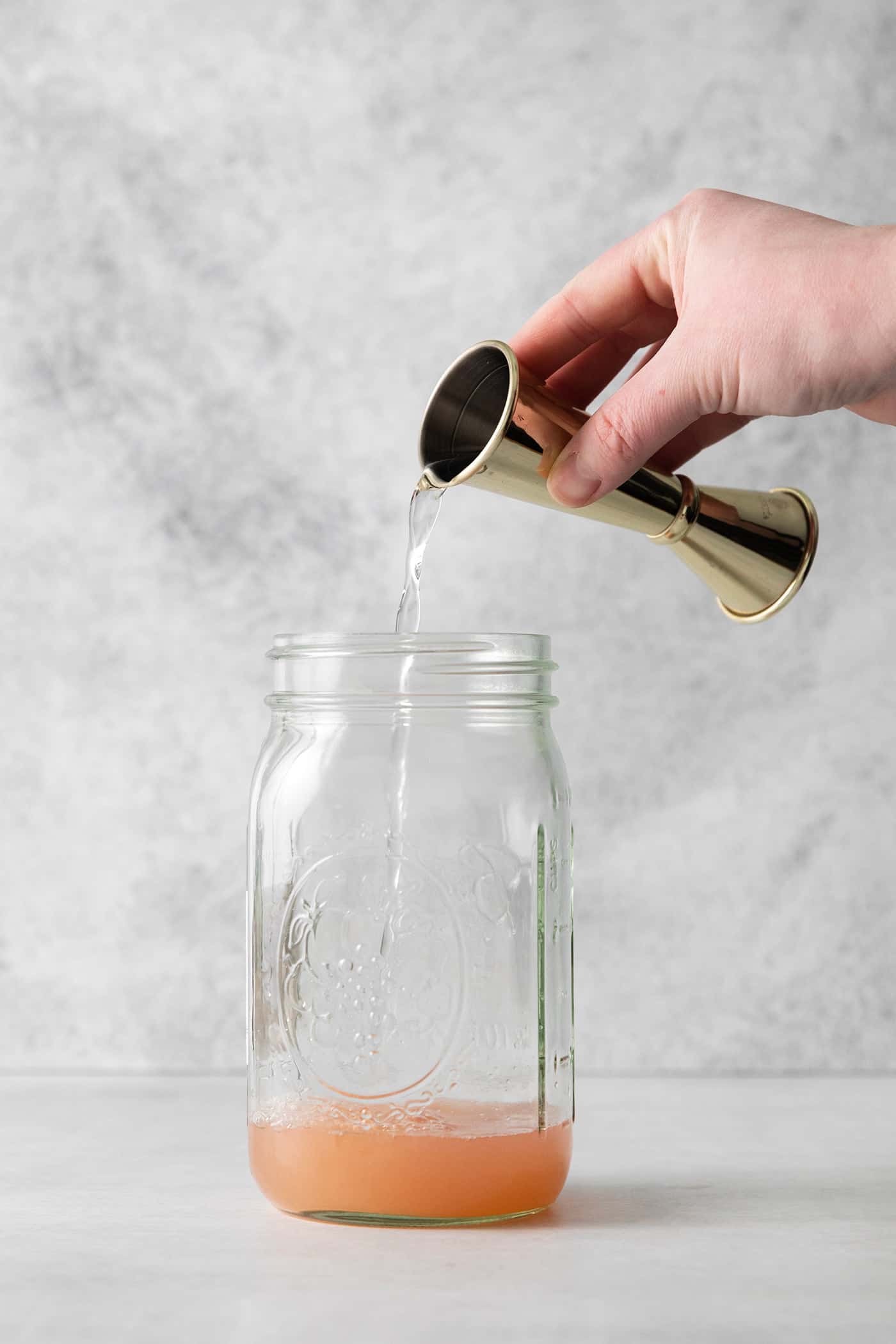 This Salty Dog cocktail is a twist on a classic greyhound that features gin and a coarse salt rim. The cocktail is fruity and refreshing. A hand pouring gin into a mason jar