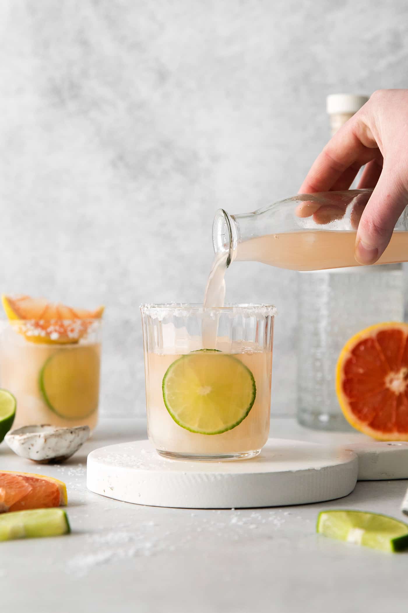 This Salty Dog cocktail is a twist on a classic greyhound that features gin and a coarse salt rim. The cocktail is fruity and refreshing. A hand pouring grapefruit cocktail in a glass over ice