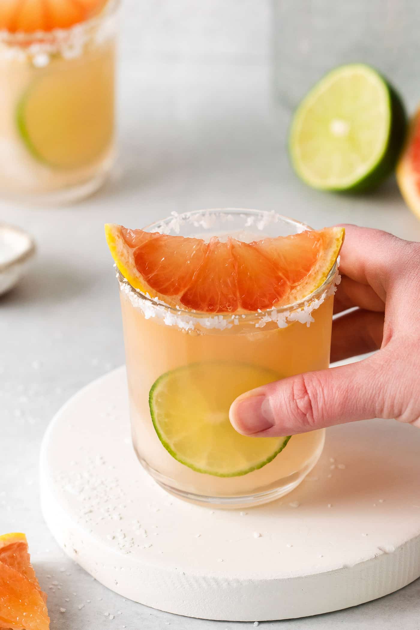 This Salty Dog cocktail is a twist on a classic greyhound that features gin and a coarse salt rim. The cocktail is fruity and refreshing. A hand holding a salty dog drink