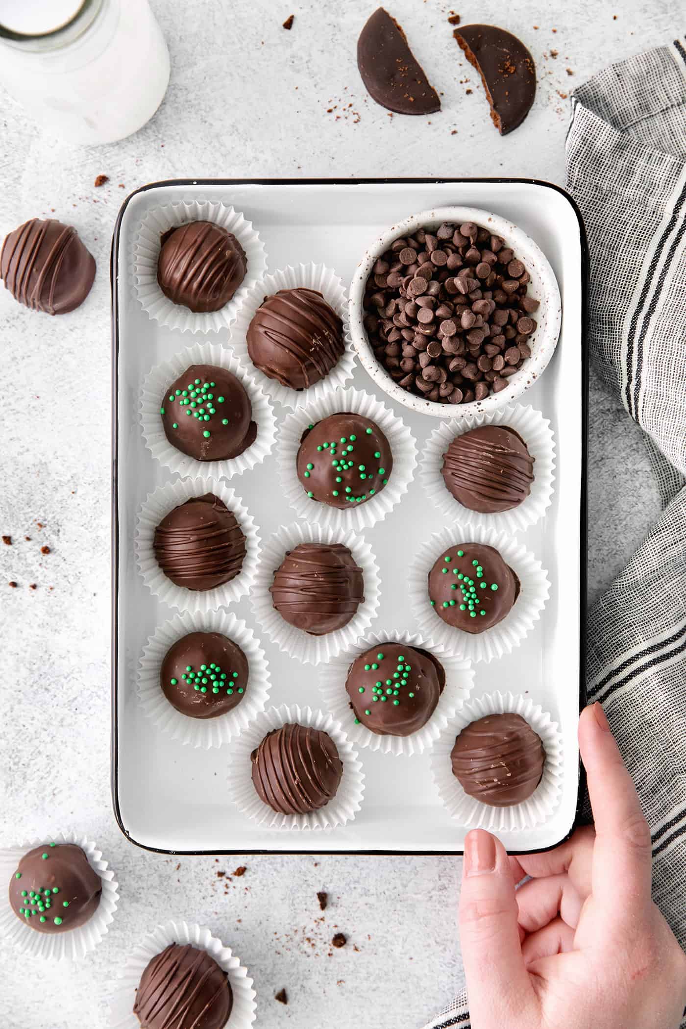 Made with your favorite Girl Scout cookies, these Thin Mint Truffles are the perfect combination of rich chocolate and mint flavor. A hand holding a tray of mint chocolate truffles