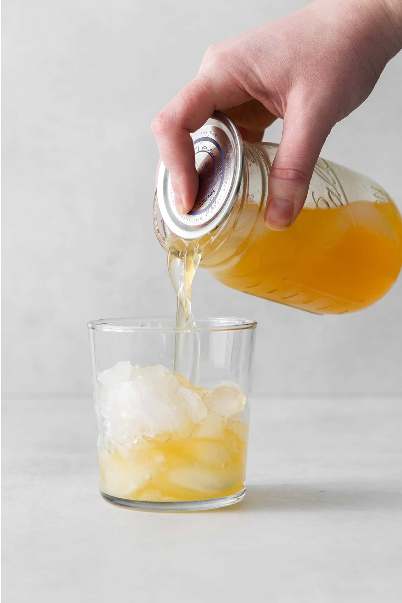 This New York Sour is made with whiskey, freshly squeezed lemon juice, simple syrup, and fruity red wine. Perfectly sweet & tart. A sour cocktail being poured from a mason jar into a cocktail glass over ice