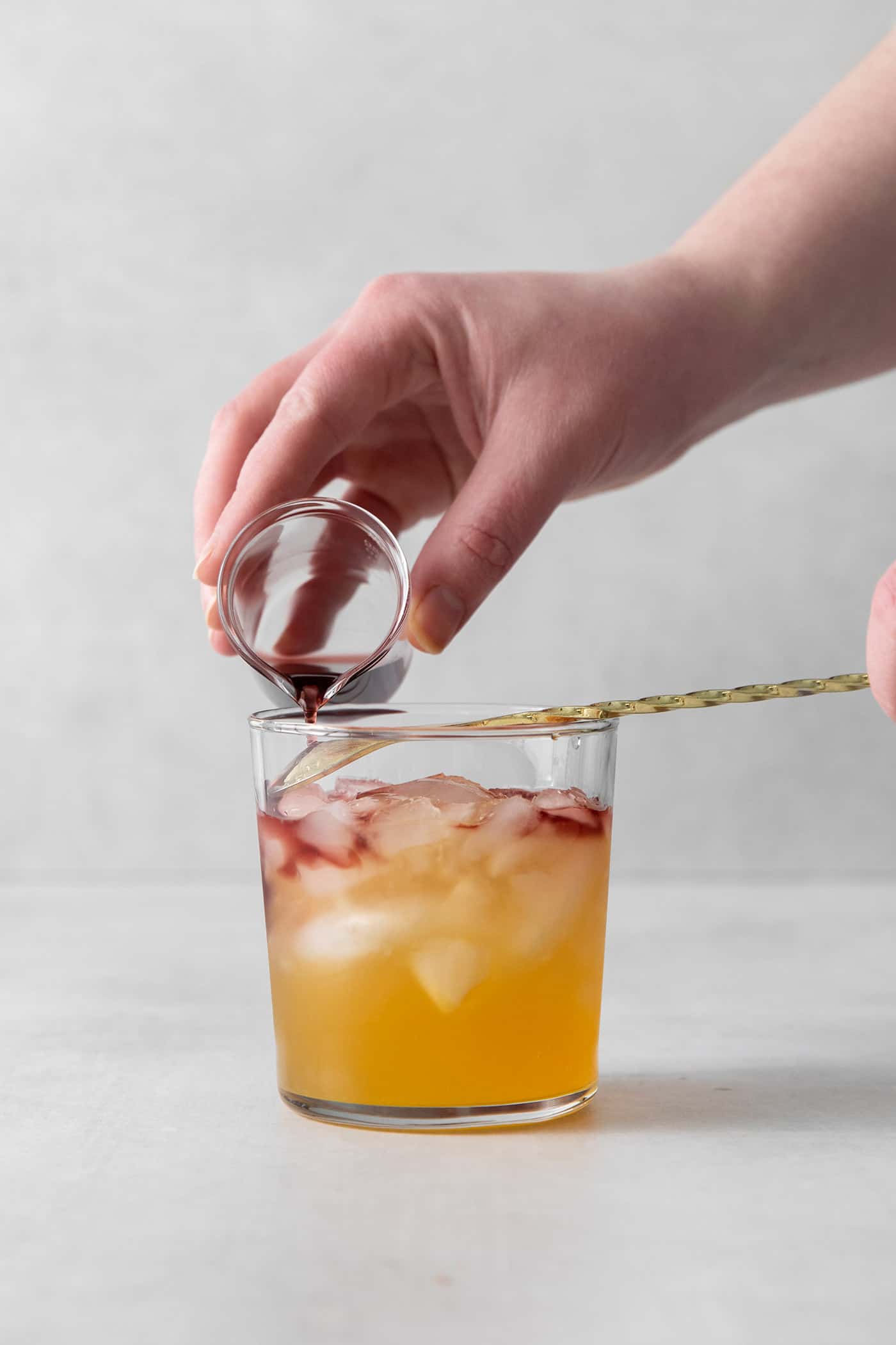 This New York Sour is made with whiskey, freshly squeezed lemon juice, simple syrup, and fruity red wine. Perfectly sweet & tart. Red wine being poured into a cocktail glass over a spoon