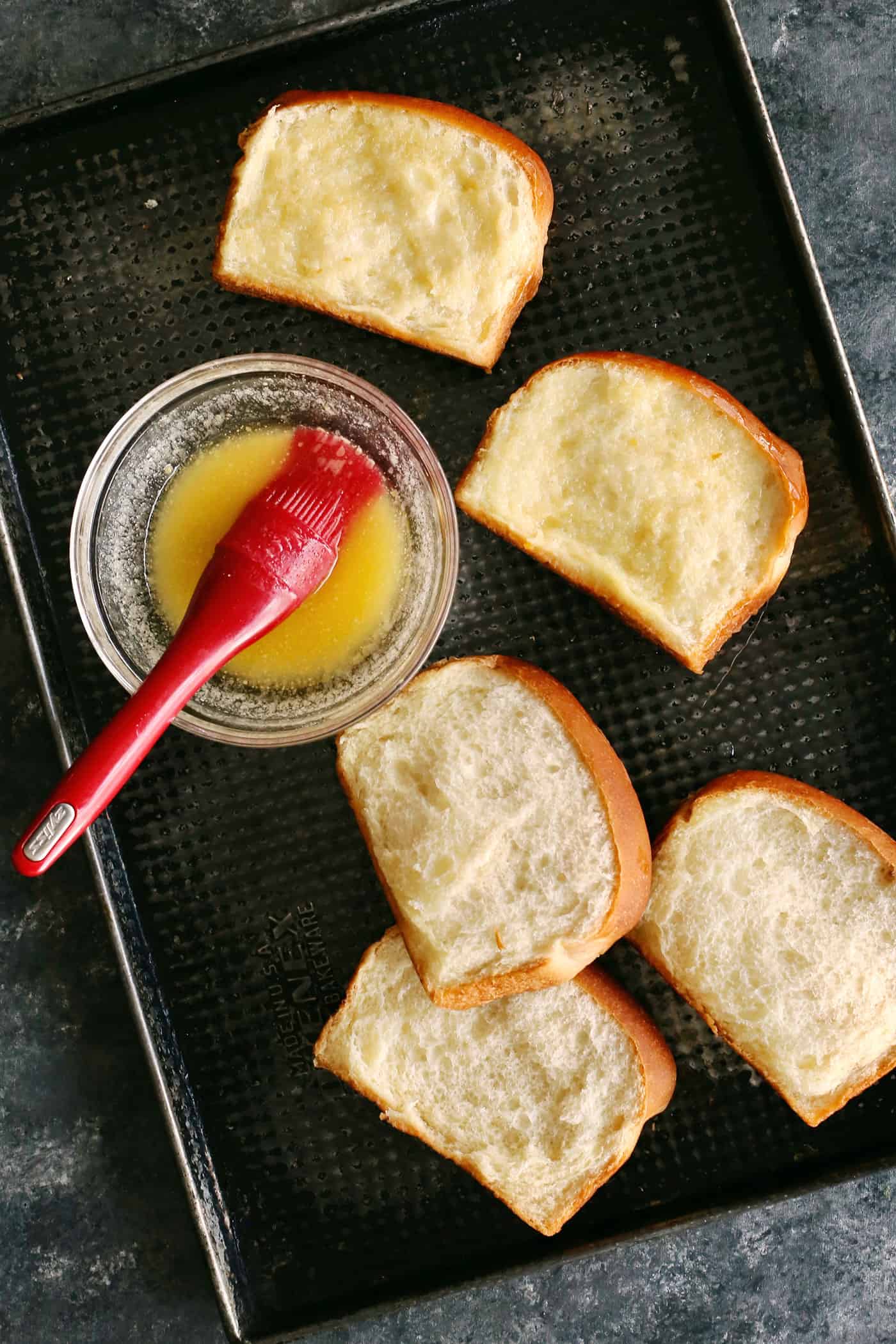 This Homemade Texas Toast Garlic Bread is made entirely on the stovetop with just 3 ingredients. It's the perfect addition to any meal. Melted butter being brushed on slices of toast