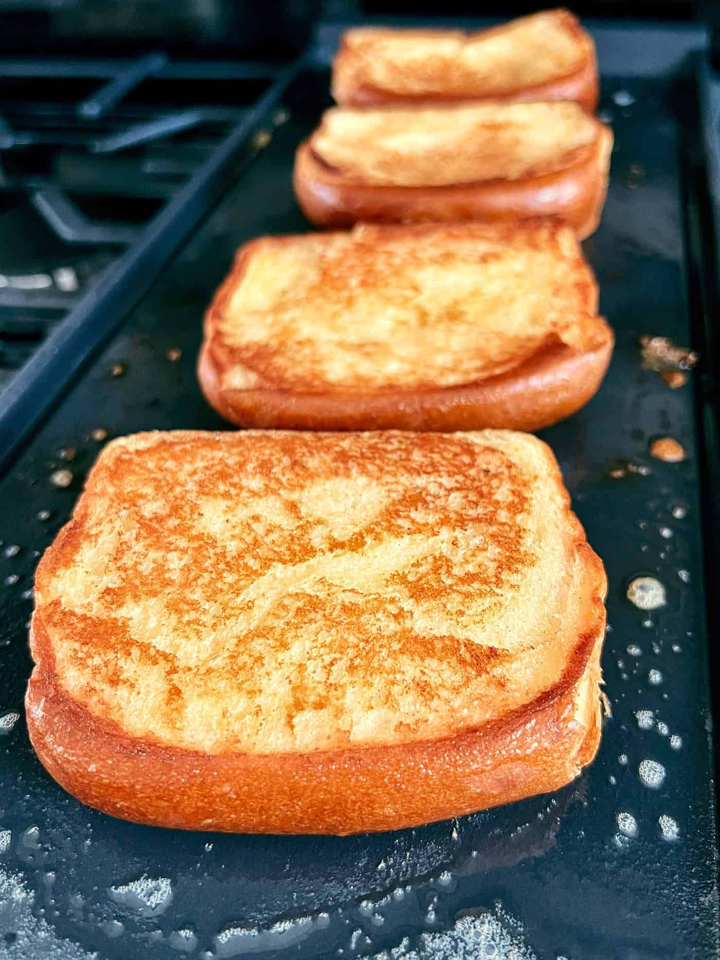 This Homemade Texas Toast Garlic Bread is made entirely on the stovetop with just 3 ingredients. It's the perfect addition to any meal. Slices of garlic bread on a griddle
