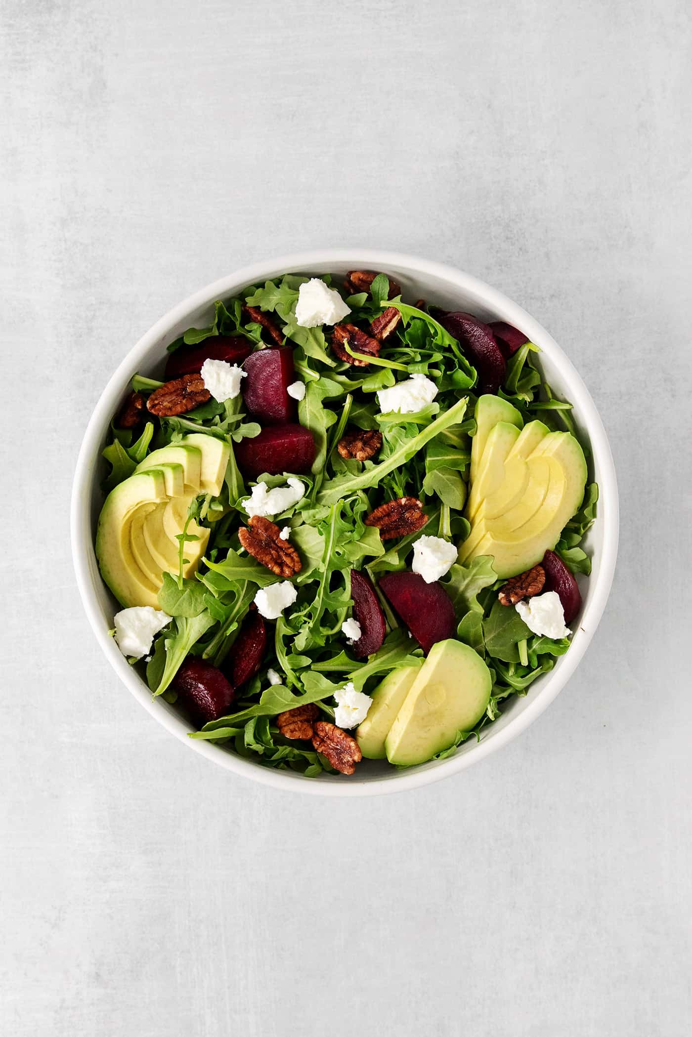 Topped with goat cheese, avocado, and candied pecans, this Arugula Beet Salad offers the perfect combination of flavors. Overhead view of a bowl of arugula beet salad