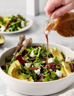 Balsamic vinaigrette being poured over arugula salad