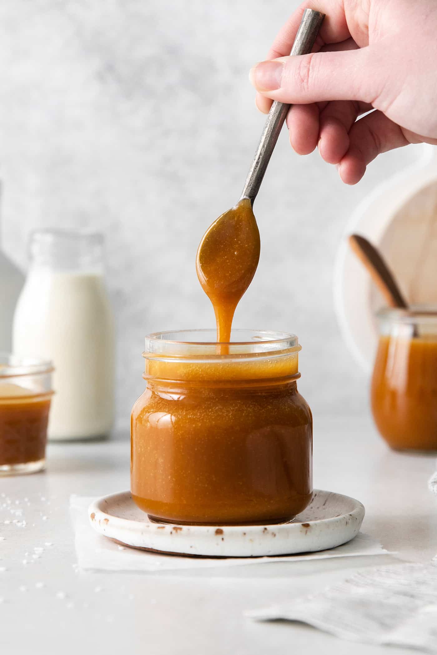 A spoon dripping caramel sauce back into the jar