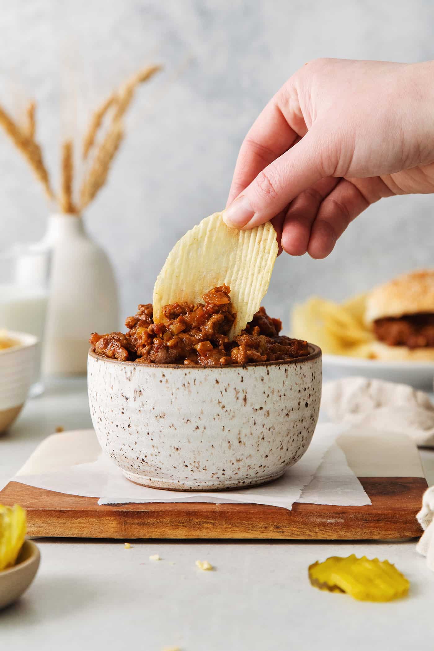 Slow Cooker Sloppy Joes are super flavorful, easy to make, and great for feeding a crowd. Serve on sandwich buns for a quick meal anytime. A hand dipping a chip in sloppy joe meat