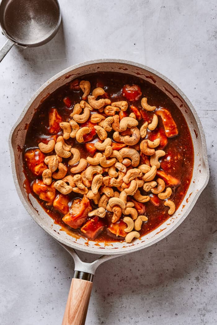 Quick, easy, and so flavorful, this Cashew Chicken stir fry features juicy pieces of chicken breast and cashews tossed in a garlic sauce. Cashews added to chicken in a frying pan