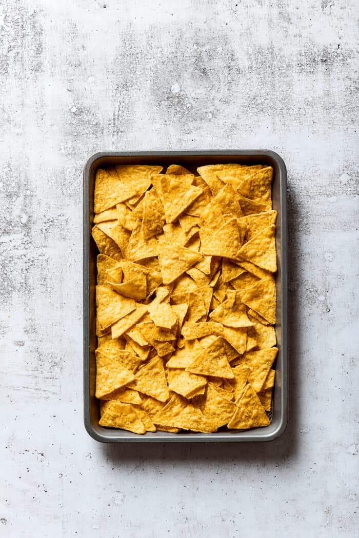 Loaded with pork, cheese, tomatoes, and all the toppings you desire, these Pulled Pork Nachos are an easy and tasty appetizer. Tortilla chips spread on a baking sheet