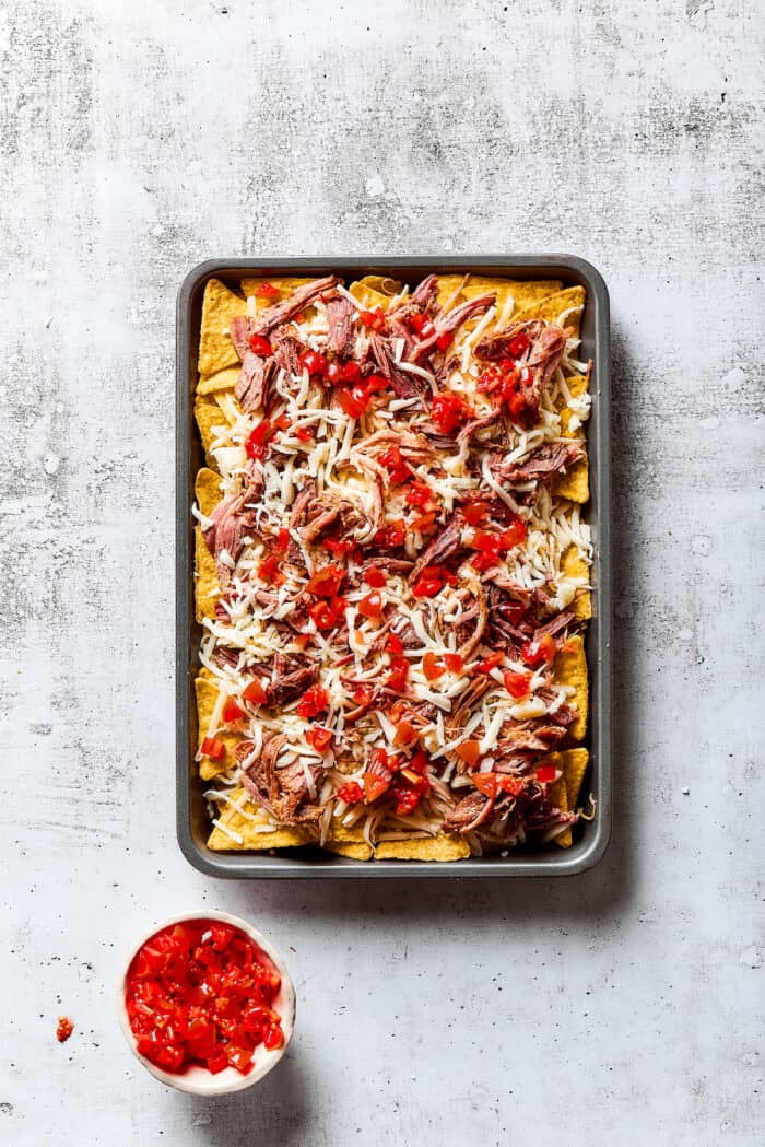 Loaded with pork, cheese, tomatoes, and all the toppings you desire, these Pulled Pork Nachos are an easy and tasty appetizer. A baking sheet of tortilla chips topped with pulled pork, shredded cheese, and diced tomatoes