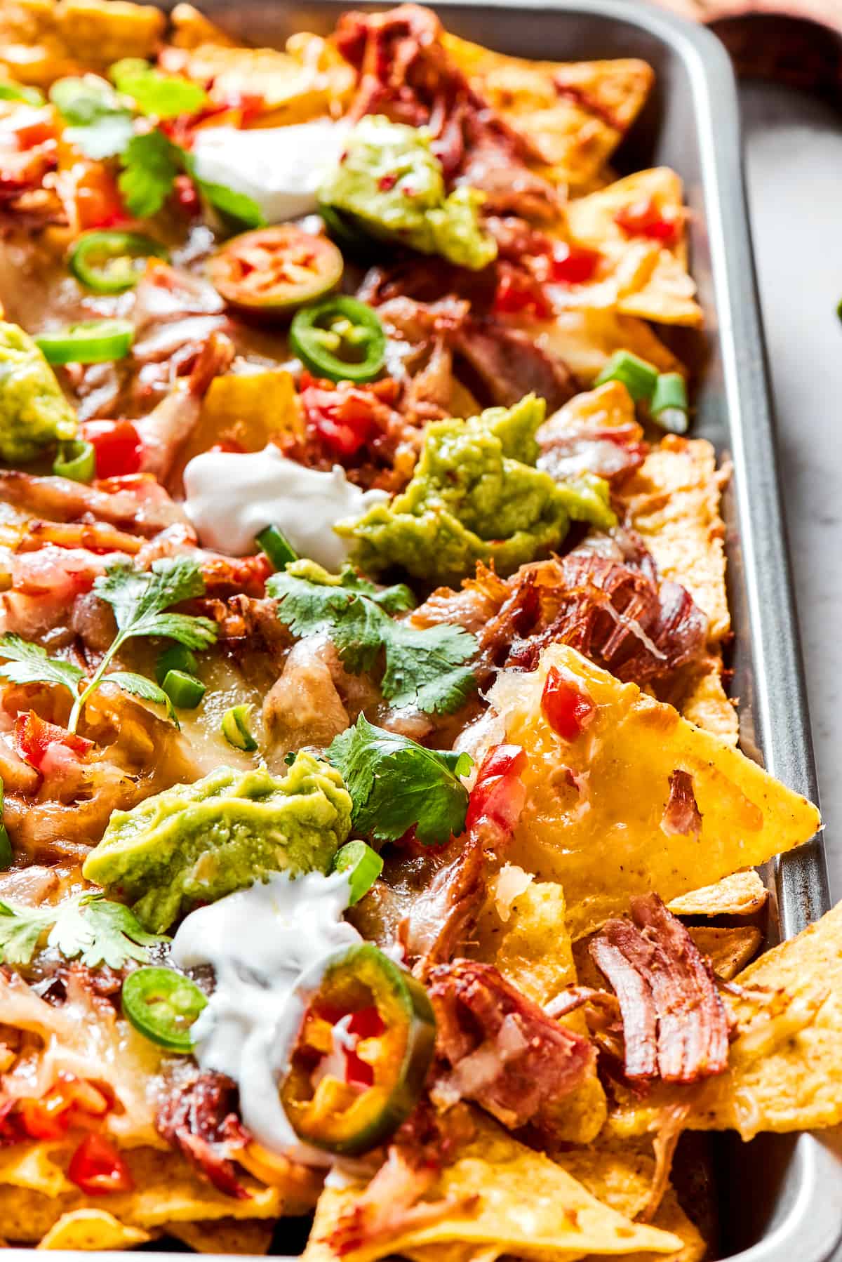 Loaded with pork, cheese, tomatoes, and all the toppings you desire, these Pulled Pork Nachos are an easy and tasty appetizer. Sheet pan of BBQ pulled pork nachos