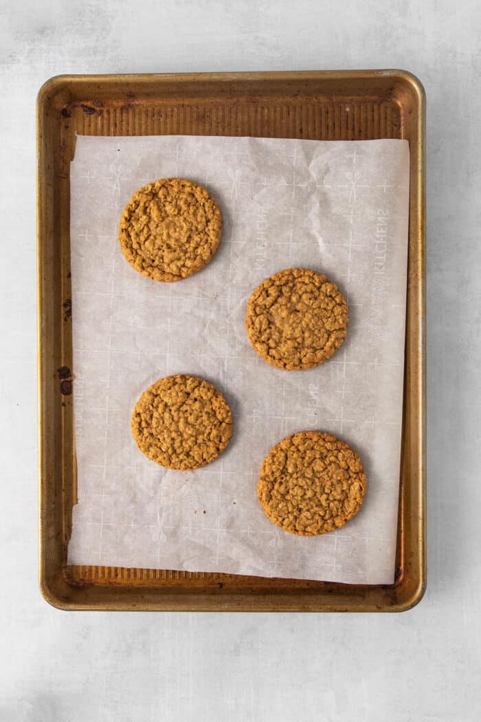 These Oatmeal Cream Pies are just like the classic store-bought variety, where a layer of sweet cream is sandwiched by chewy oatmeal cookies. Baked oatmeal cookies on a baking sheet
