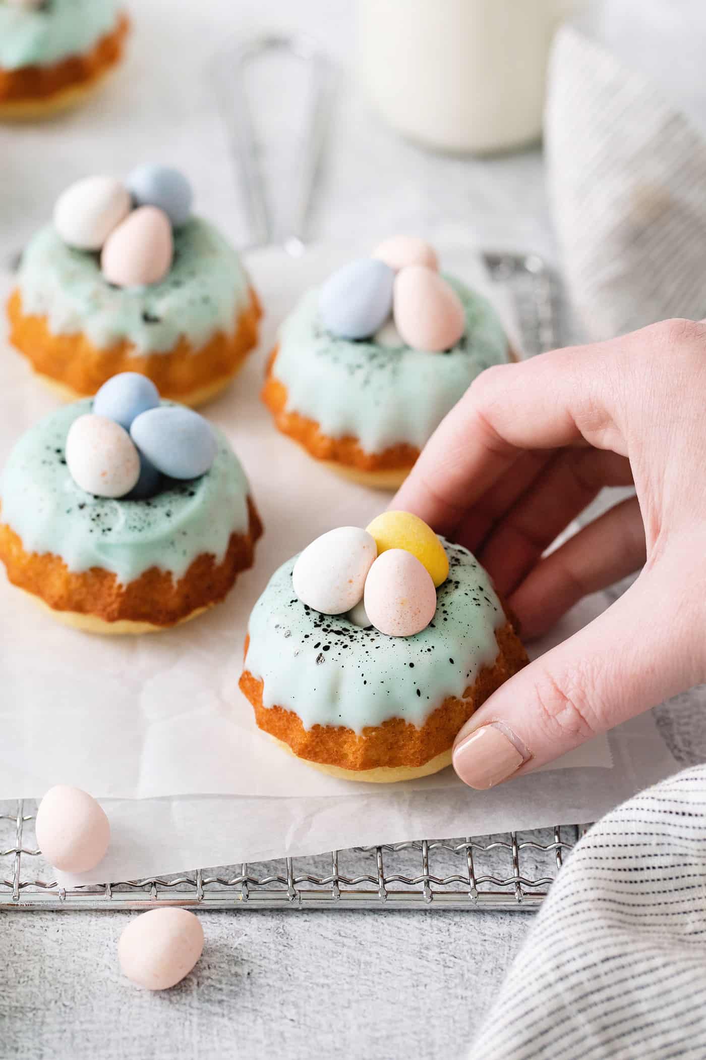 These Robin’s Egg Mini Bundt Cakes are the perfect sweet springtime treat. A moist, vanilla cake topped with a sweet glaze! A hand grabbing a mini bundt cake