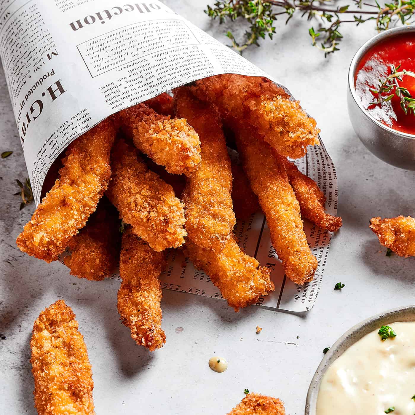 These Chicken Fries feature thin, tender strips of chicken breast with a flavorful, crispy exterior, plus roasted garlic aioli for dipping! close-up photo of chicken fries in a newspaper cone