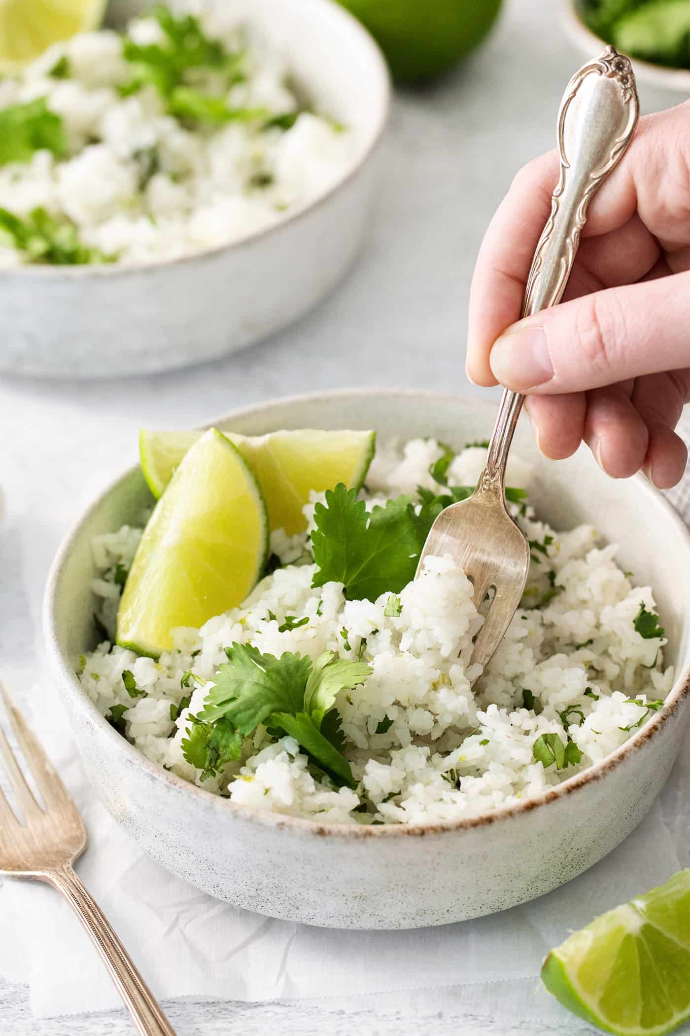 Cilantro Lime Rice is the perfect base or side for so many recipes. The rice is perfectly cooked and seasoned with hints of lime & cilantro. A fork diving into a bowl of cilantro lime rice