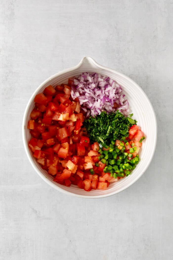 Made with ripe tomatoes, red onion, and lime juice, Homemade Pico de Gallo is the perfect garnish for anything from tacos to scallop bowls! Pico de gallo ingredients in a bowl