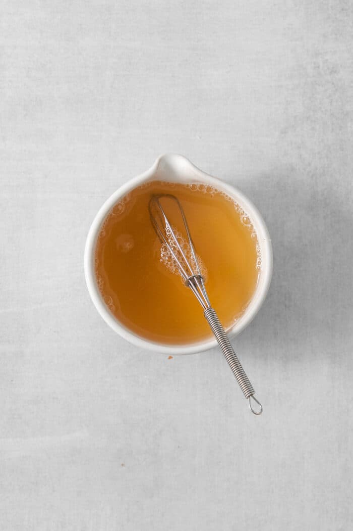 Honey and water are whisked in a white bowl.