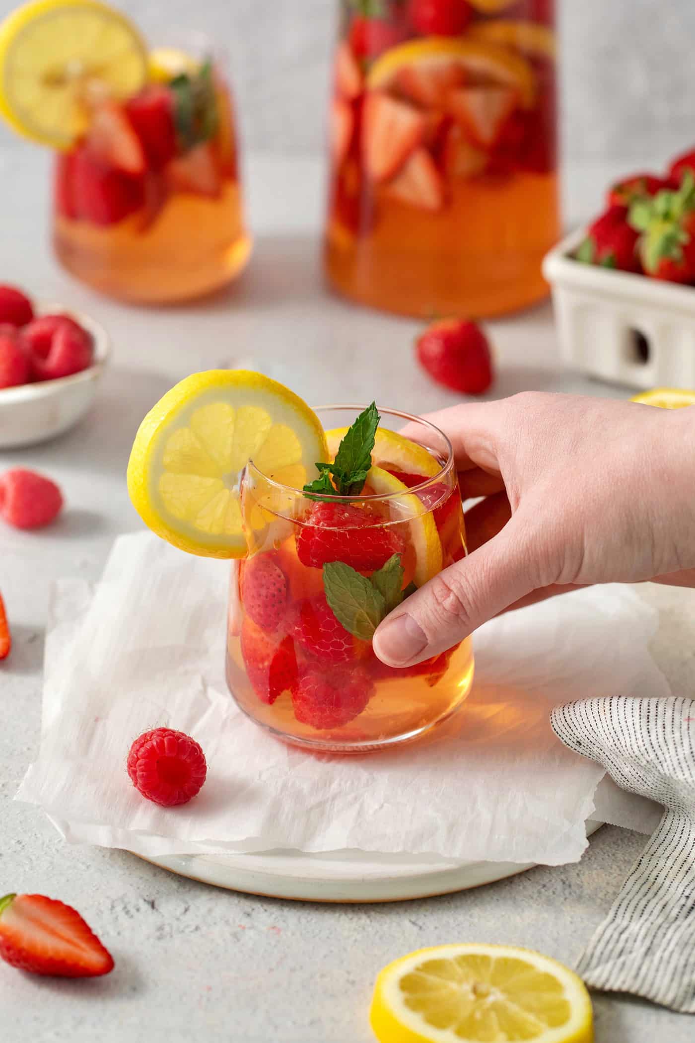 A hand places a glass of rose sangria on a table.