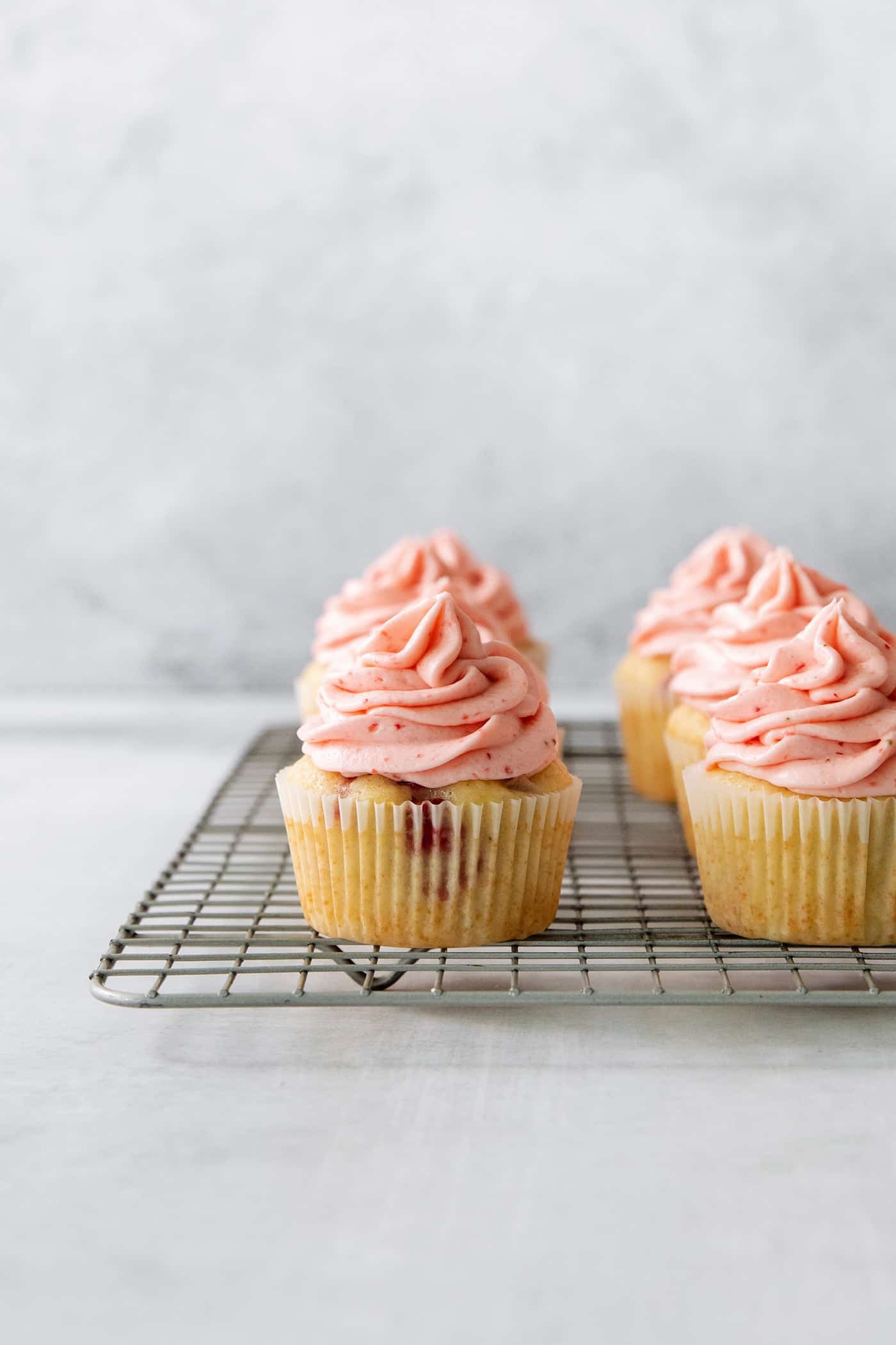 Vibrantly pink Strawberry Cupcakes will dress up your Mother's Day table - or make them anytime for a special strawberry treat. A wire rack with three strawberry cupcakes on it.
