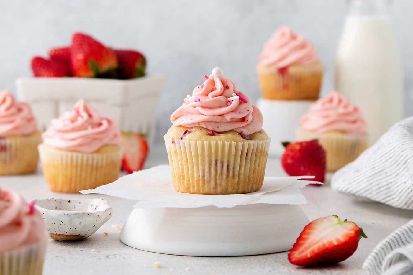 Vibrantly pink Strawberry Cupcakes will dress up your Mother's Day table - or make them anytime for a special strawberry treat. A focused shot of a strawberry cupcake with pink frosting with cupcakes and strawberries in the background.