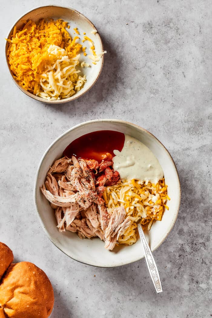 Buffalo Chicken Sliders are hand-held bites of spicy goodness! Loaded with melted cheese and creamy ranch, these are sure to be a hit. Mixing the ingredients for buffalo chicken sliders in a bowl.