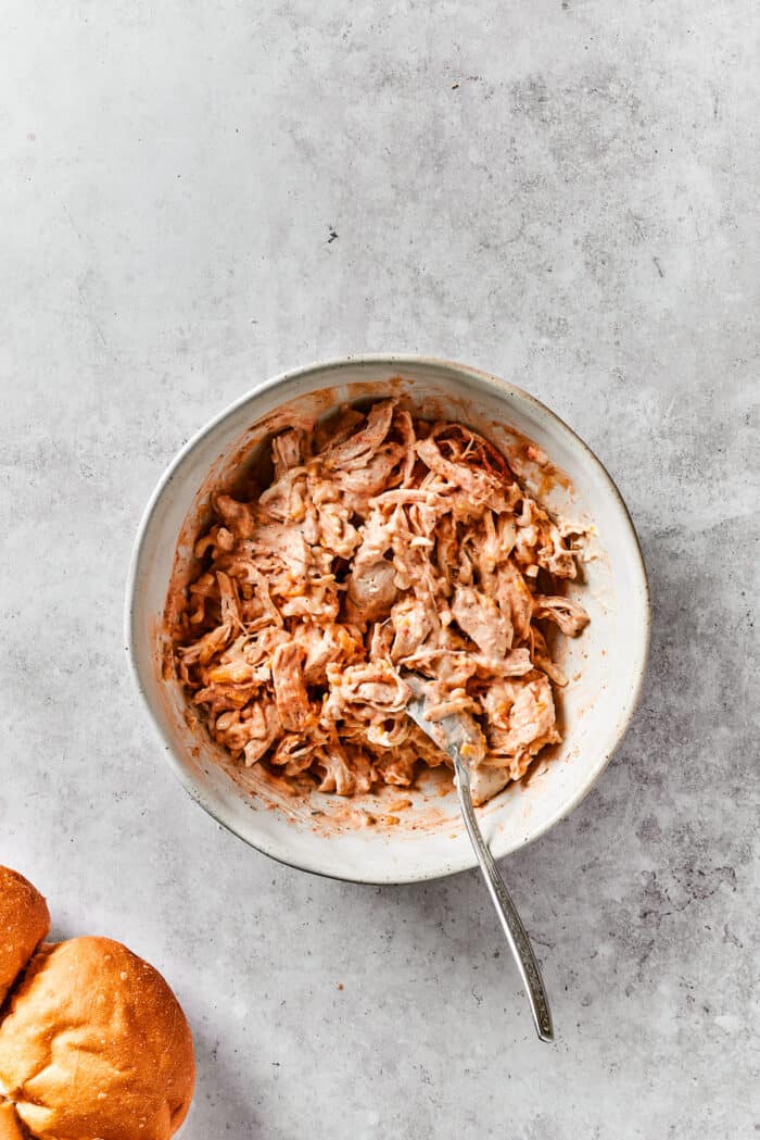 Buffalo Chicken Sliders are hand-held bites of spicy goodness! Loaded with melted cheese and creamy ranch, these are sure to be a hit. Mixing ranch into shredded chicken.
