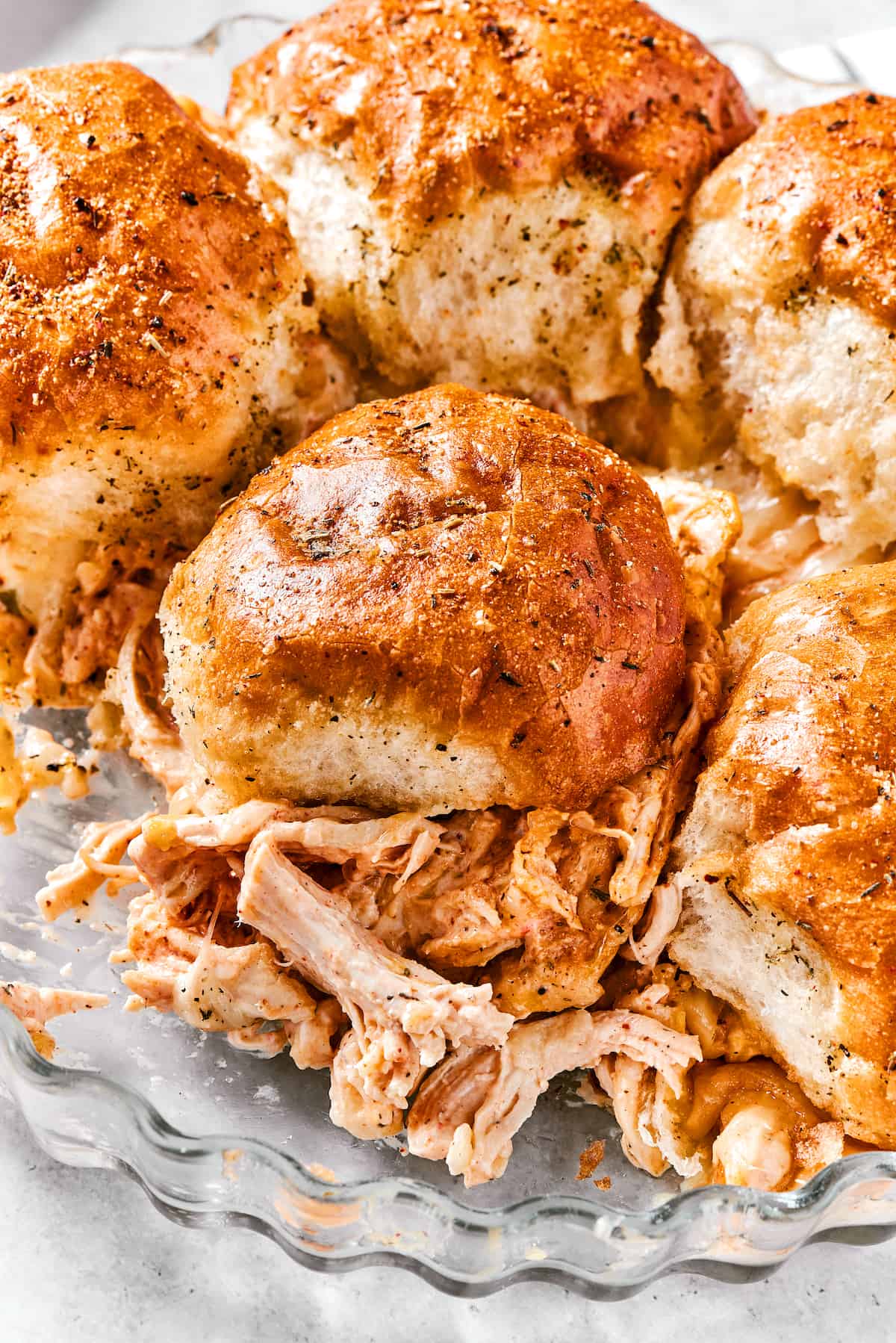 Buffalo Chicken Sliders are hand-held bites of spicy goodness! Loaded with melted cheese and creamy ranch, these are sure to be a hit. Buffalo chicken sliders are shown in a metal dish.