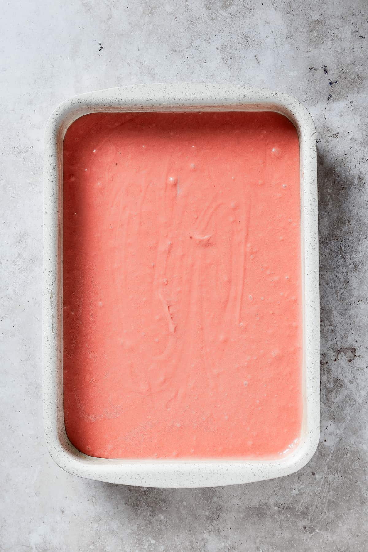 Creamy and sweet with a bit of crunch, Strawberry Crunch Cake is bursting with fruit flavor! This bright strawberry dessert is a favorite. Pink strawberry crunch cake batter is shown in a white pan.