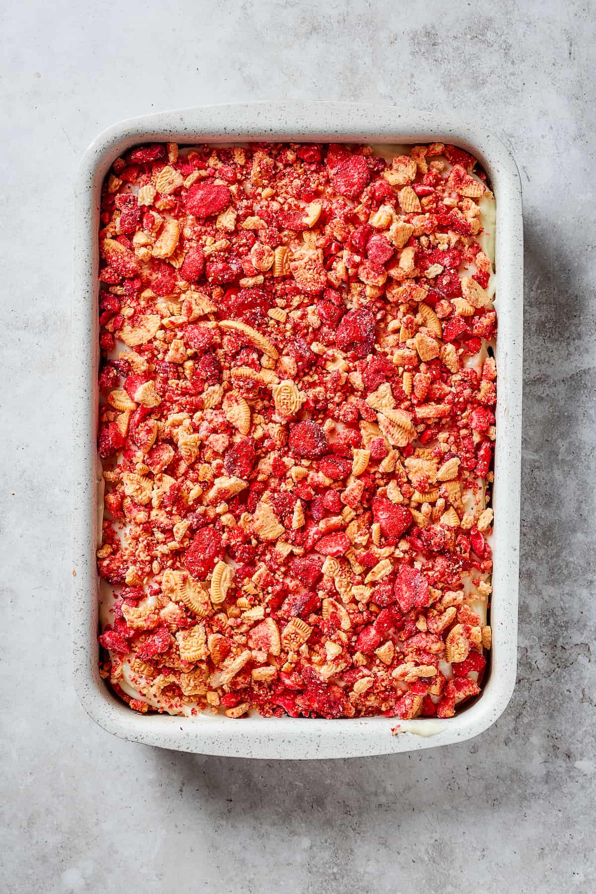Creamy and sweet with a bit of crunch, Strawberry Crunch Cake is bursting with fruit flavor! This bright strawberry dessert is a favorite. A finished strawberry crunch cake is shown in a pan.