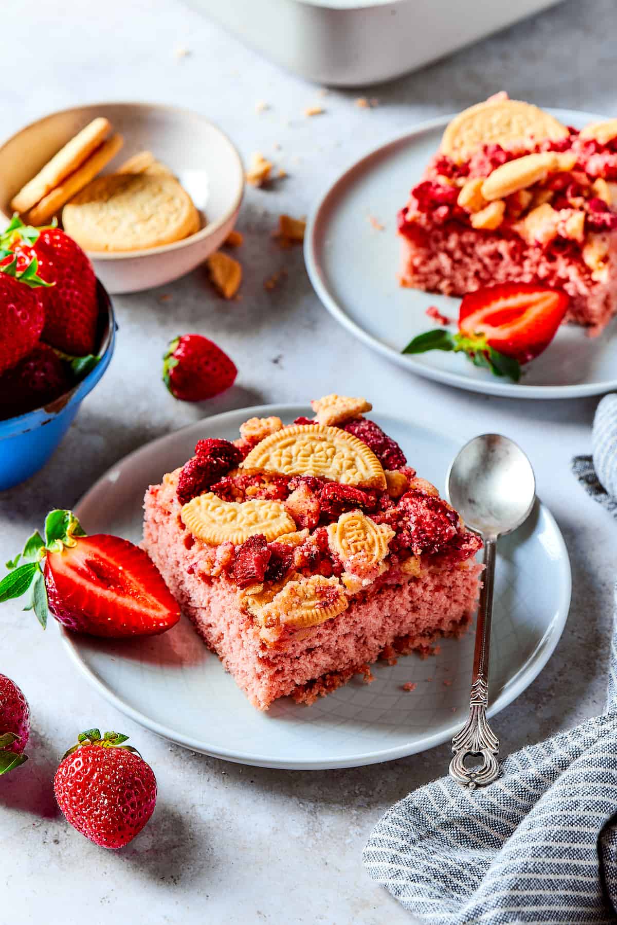 Creamy and sweet with a bit of crunch, Strawberry Crunch Cake is bursting with fruit flavor! This bright strawberry dessert is a favorite. Pieces of strawberry crunch cake on plates with strawberries in bowls.