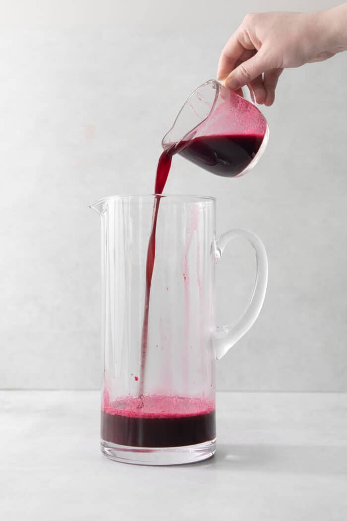 This Blueberry Lemonade is the perfect summertime drink! It’s fruity and refreshing with tart lemons and sweet blueberries. A cup pouring blueberry syrup into a pitcher