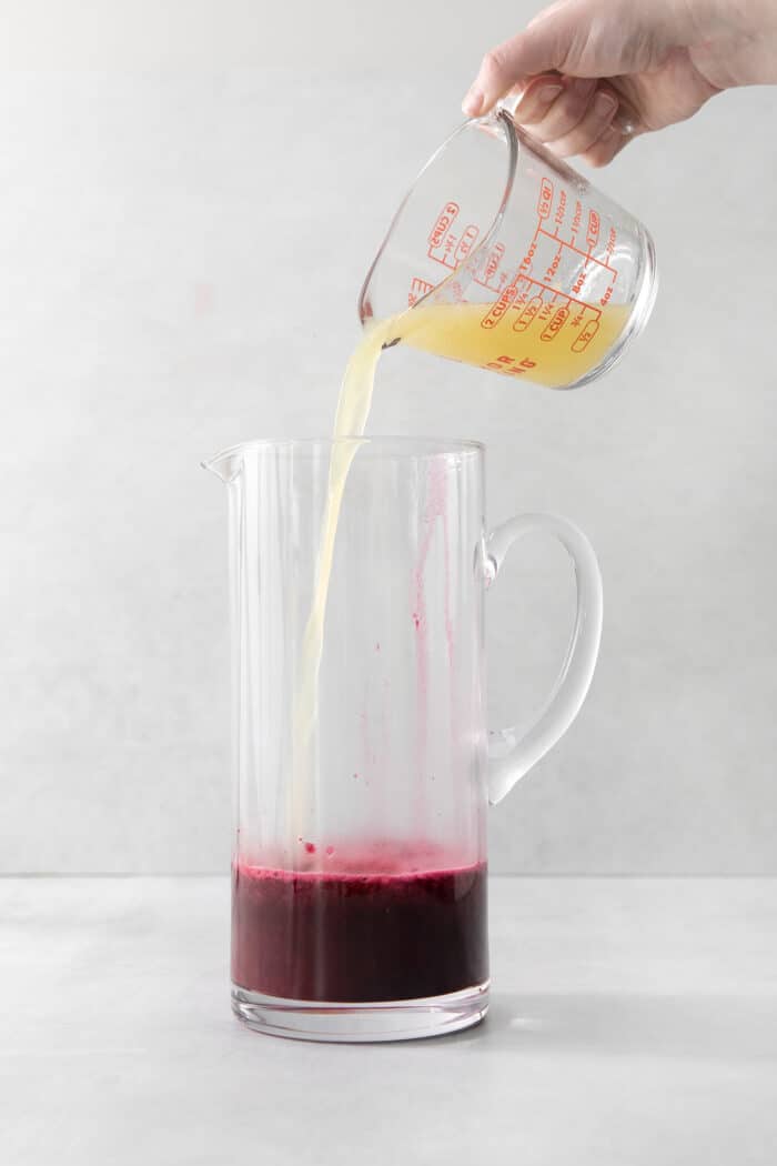 This Blueberry Lemonade is the perfect summertime drink! It’s fruity and refreshing with tart lemons and sweet blueberries. Lemon juice being added to a pitcher with blueberry syrup