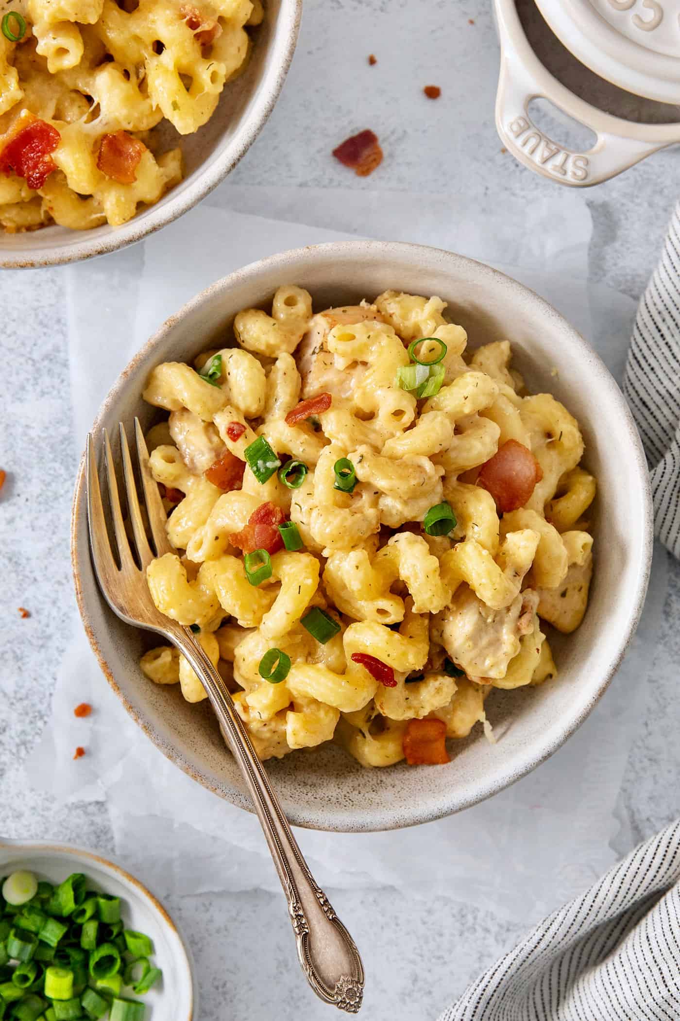 This Chicken Bacon Ranch Pasta is a perfect family-friendly meal loaded with flavor! Bacon, chicken, and pasta are baked in a creamy sauce. A bowl of chicken bacon ranch pasta on a white background with a fork.