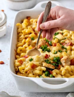 A hand holding a spoon digs into a casserole dish of chicken bacon ranch pasta.