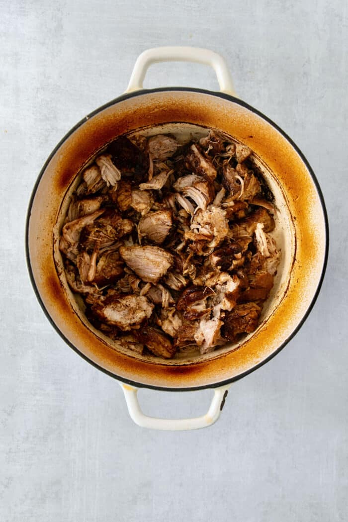 Incredibly tender and a little bit spicy, this easy Pulled Pork recipe is an absolute keeper. It's also super flavorful and versatile. Cooked pork is shown in a Dutch Oven.