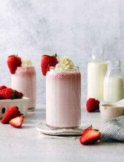 Glasses of strawberry milk with milk in the background.