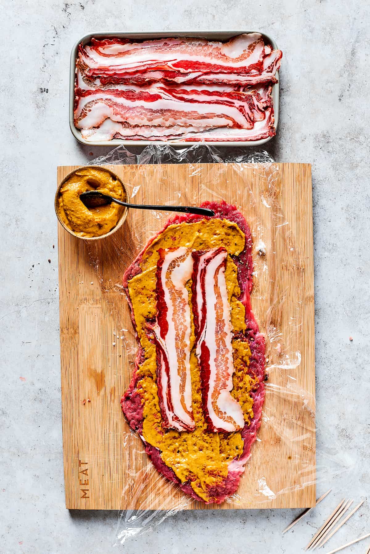 Rich, flavorful Rouladen is a classic German dish. Little meat rolls are stuffed with onions, bacon, and pickles then simmered in gravy. Adding bacon and mustard to a beef strip.