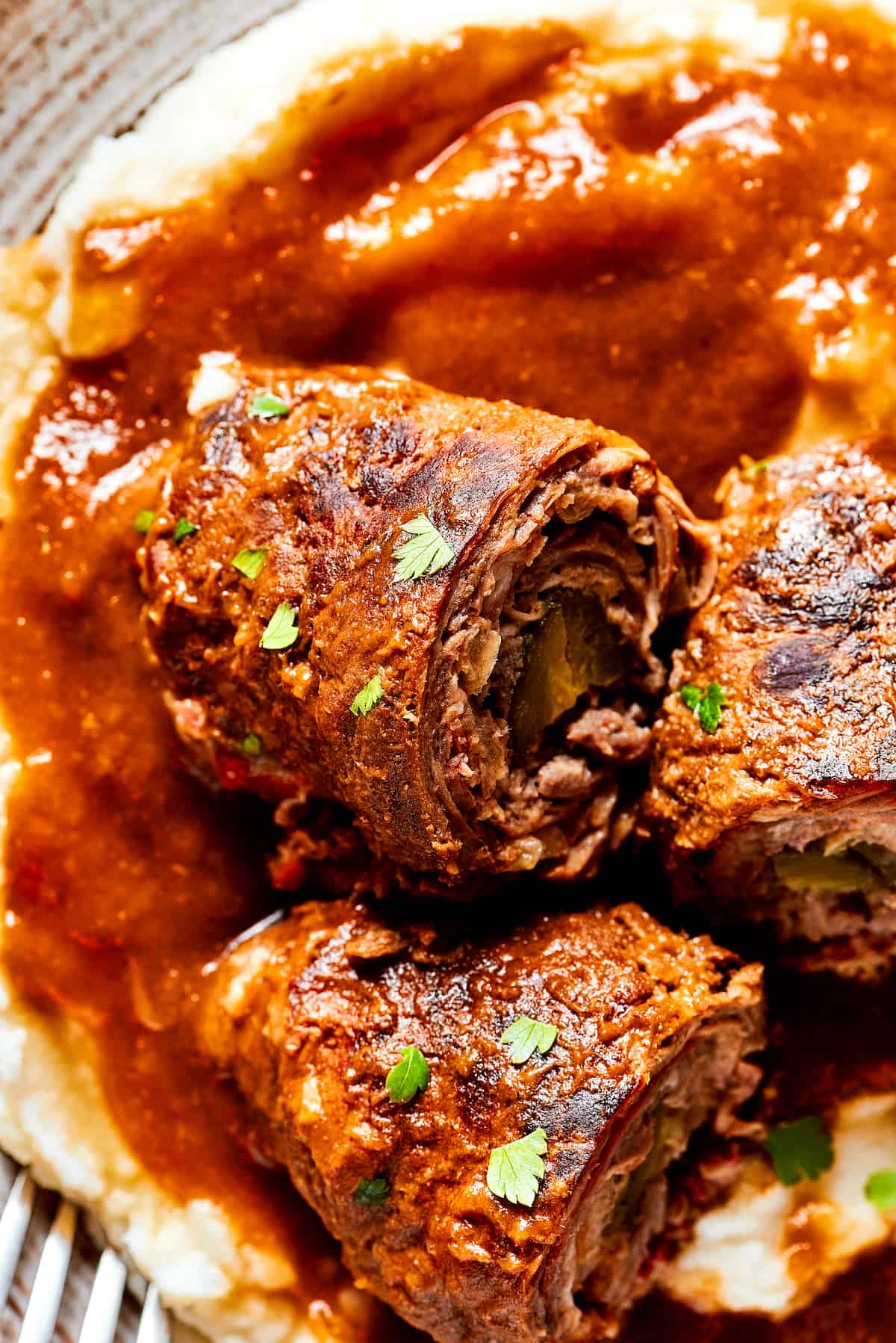 Rich, flavorful Rouladen is a classic German dish. Little meat rolls are stuffed with onions, bacon, and pickles then simmered in gravy. Close up of German rouladen.
