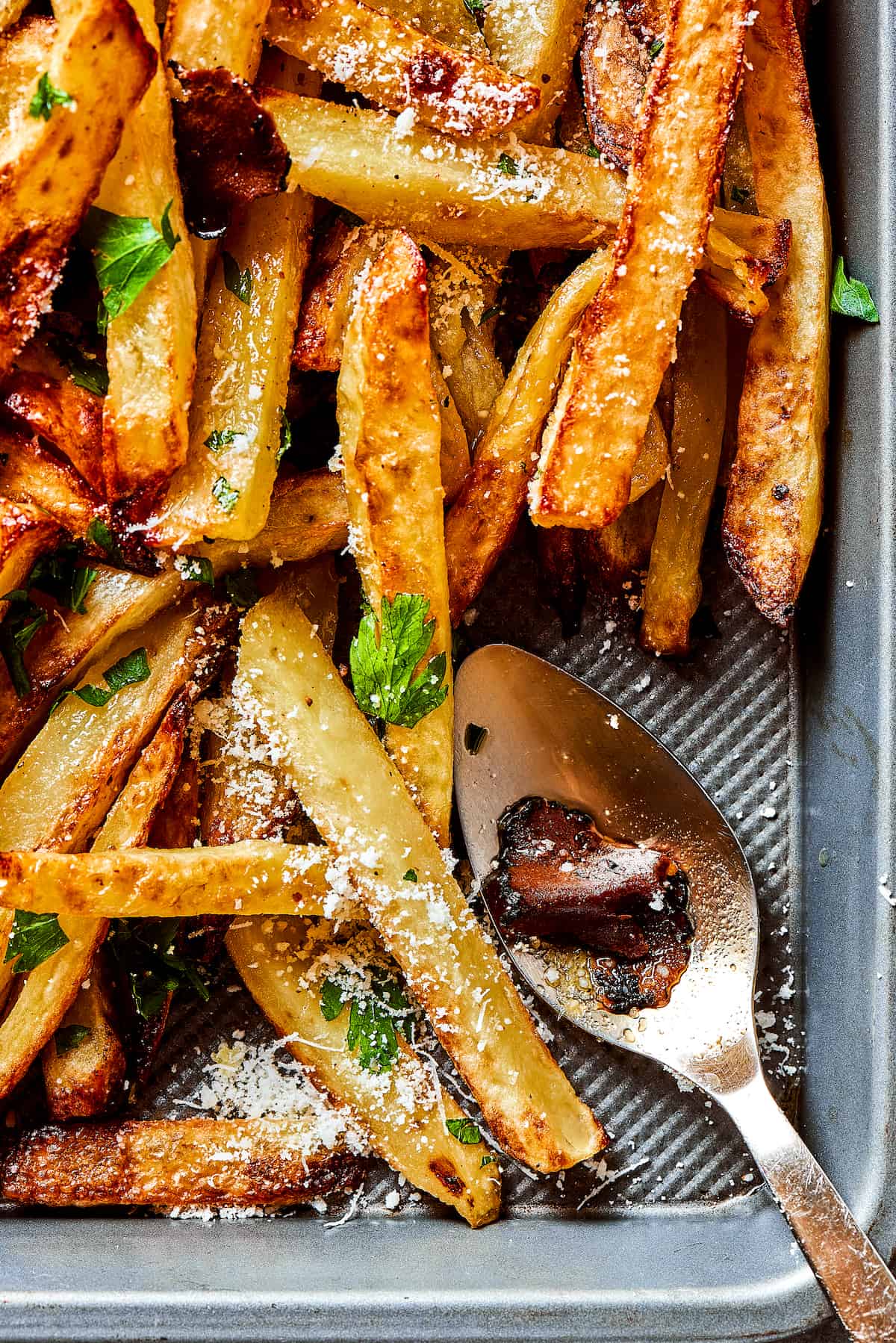 Crispy and flavorful, Truffle Fries may become your new favorite fry! They're touched with truffle salt and a dusting of parmesan cheese. A tray of truffle fries with a spoon.