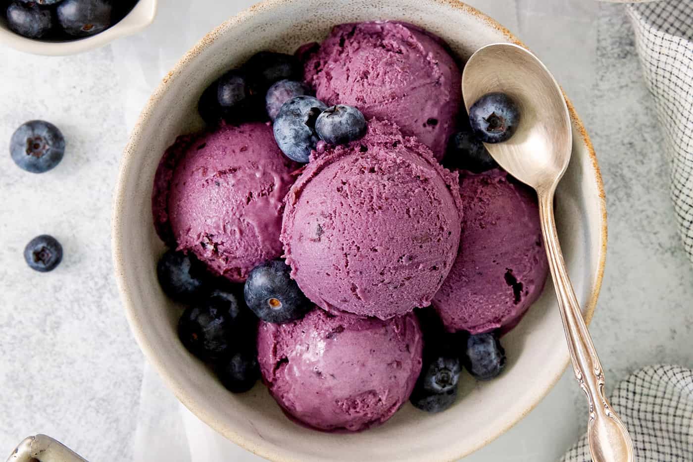 Summer-sweet Crème Fraîche Blueberry Ice Cream swirls roasted blueberries into a creamy ice cream to make the best of blueberry season! A bowl of scoops of blueberry ice cream with a spoon.