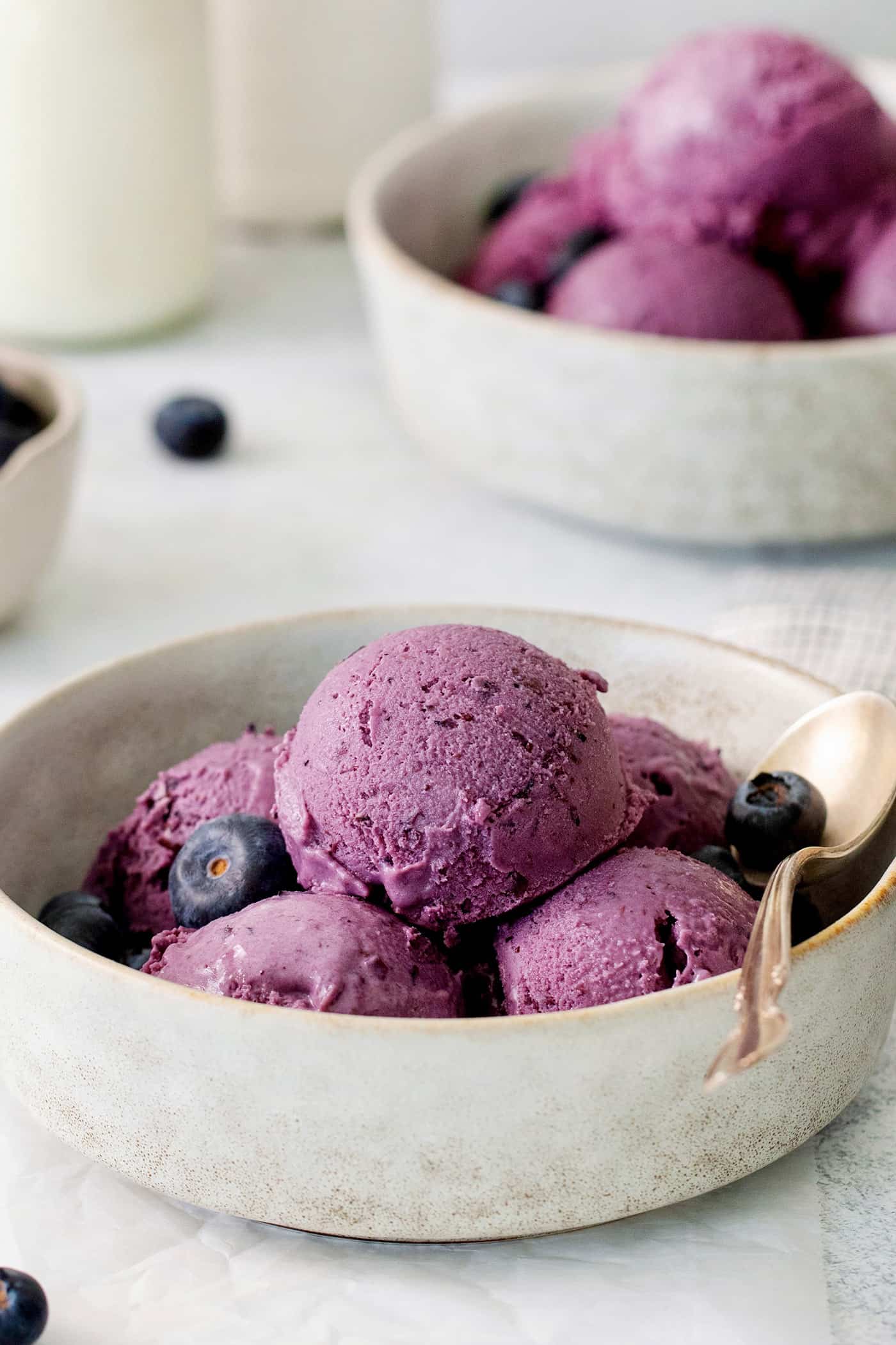 Summer-sweet Crème Fraîche Blueberry Ice Cream swirls roasted blueberries into a creamy ice cream to make the best of blueberry season! Scoops of blueberry ice cream in a white bowl.
