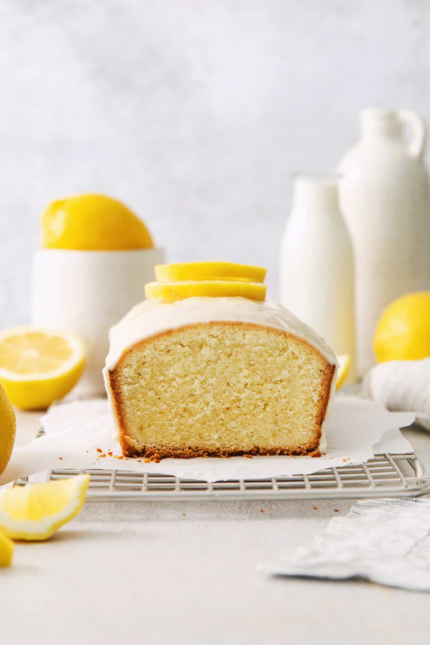 A lemon pound cake on a wire rack with lemons in the background.