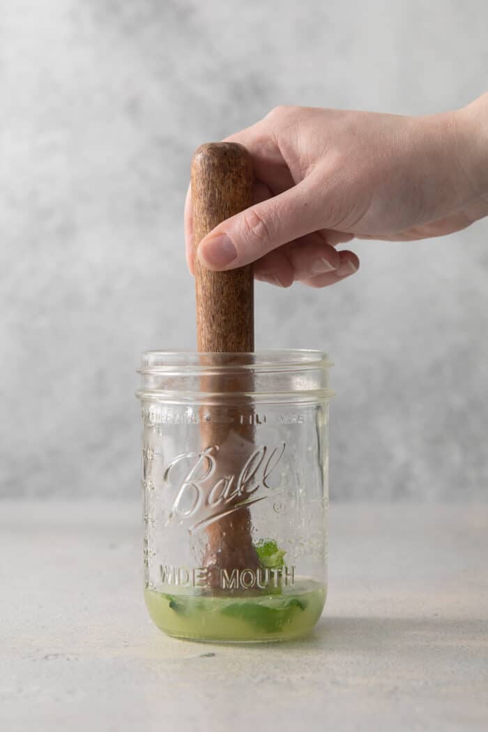 Crisp and refreshing, a Classic Mojito is the only mojito recipe you truly need! Lime juice, mint, and rum make this wonderful cocktail. A hand holding a pestle muddles mint.
