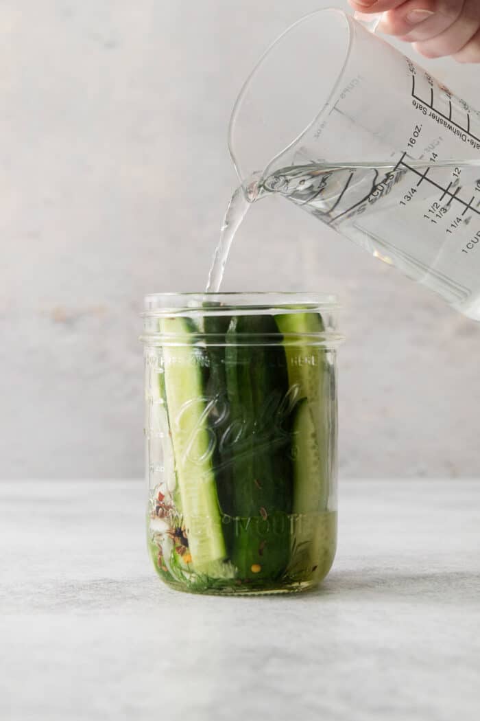 These Refrigerator Dill Pickles require no canning or special equipment, just cucumbers and a simple pickling brine. An easy side or snack! Pickling brine being poured into a jar over cucumber spears